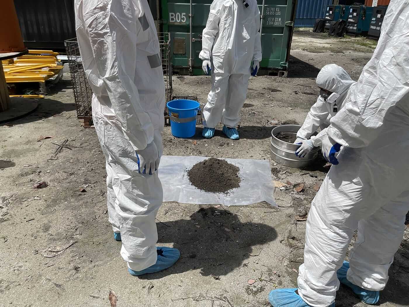 A NATA Accredited group of people in protective suits standing around a pile of soil samples, conducting asbestos testing.
