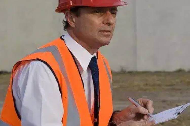 A licensed asbestos assessor in a hard hat holding a clipboard.