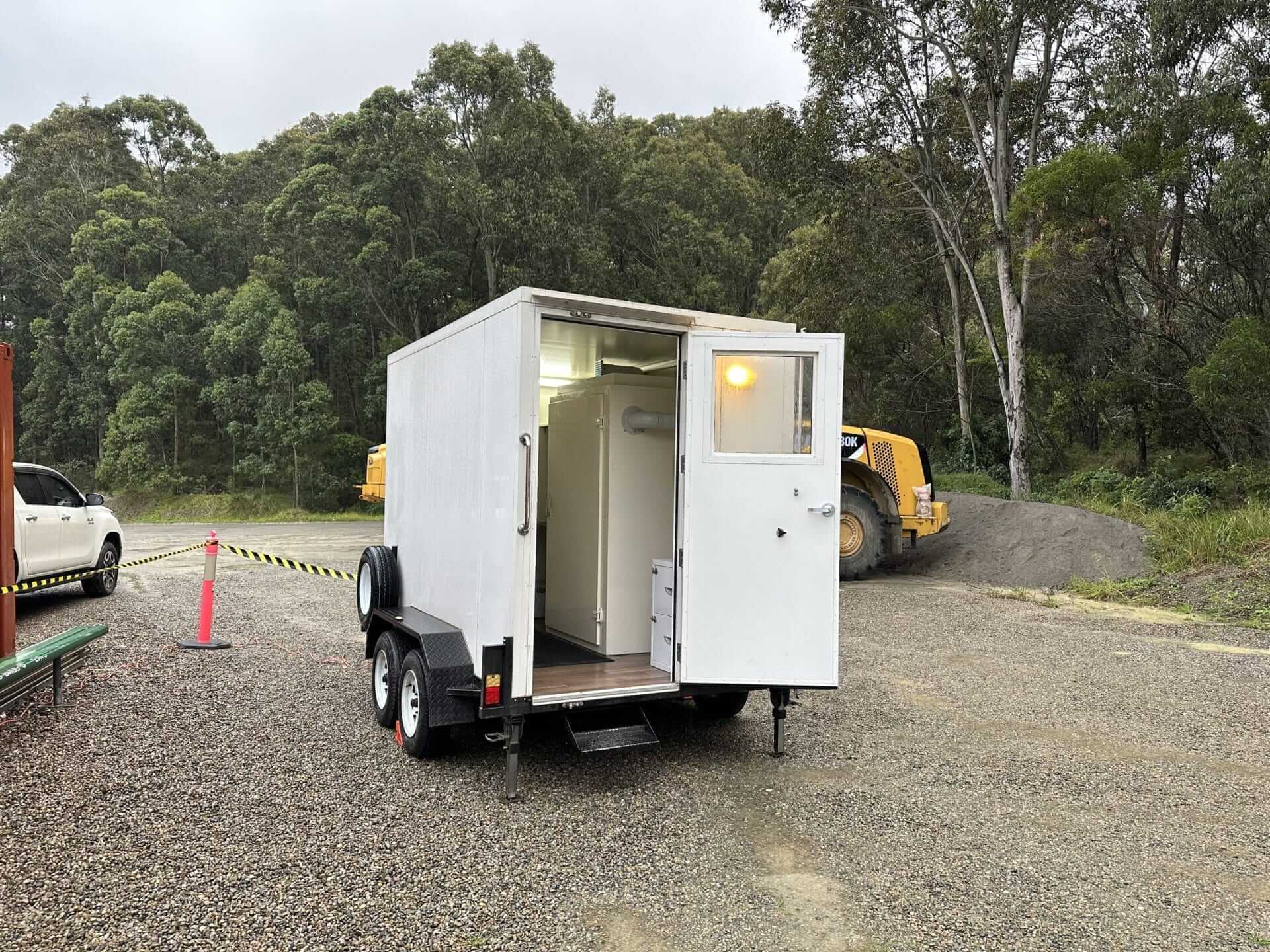 A small trailer with a toilet inside, suitable for Asbestos Testing and E. coli & Coliforms Testing.