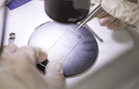 A person is using a microscope to inspect a piece of metal for NATA Accredited testing.